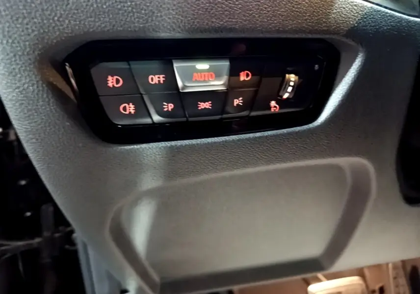Gros plan sur le panneau de commande d'éclairage noir avec boutons rétroéclairés rouges dans une BMW Série 3 318i 2022.