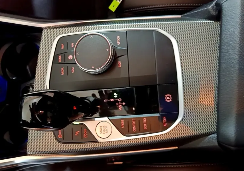 Gros plan sur la console centrale de la BMW Série 3 noire, mettant en valeur le levier de vitesses et les commandes de mode de conduite.