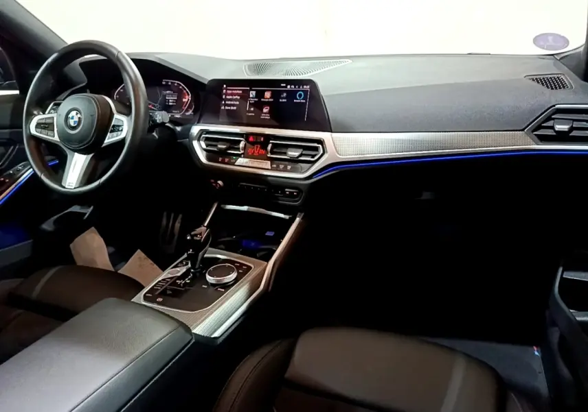 Intérieur BMW Série 3 318i 2022 vu côté conducteur, tableau de bord moderne avec éclairage d'ambiance bleu