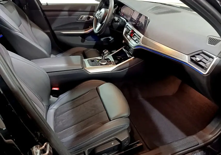 Intérieur noir de la BMW Série 3 318i 2022, vue côté conducteur, avec tableau de bord digital et éclairage d'ambiance bleu.