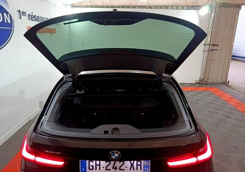 Vue arrière d'une BMW Série 3 noire 318i M Sport 2022 avec coffre ouvert et feux arrière LED allumés.