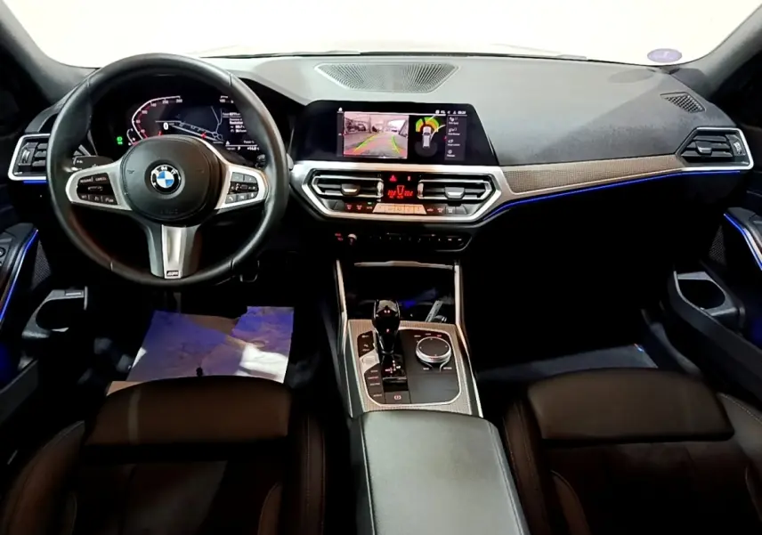 Vue intérieure avant de la BMW Série 3 318i M Sport 2022 avec tableau de bord numérique et éclairage d'ambiance bleu.