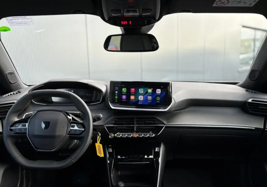 Vue frontale de l'habitacle noir du Peugeot 2008 Hybrid 145 avec écran tactile et volant compact cuir.