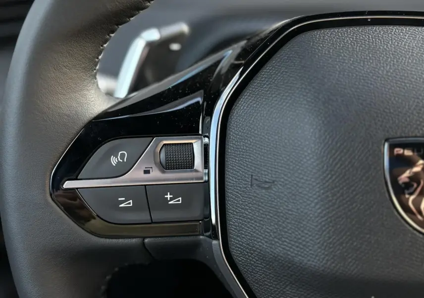 Gros plan sur les commandes multimédia gauche du volant cuir noir du Peugeot 2008 Hybrid 145 e-DSC6 Allure 2025.