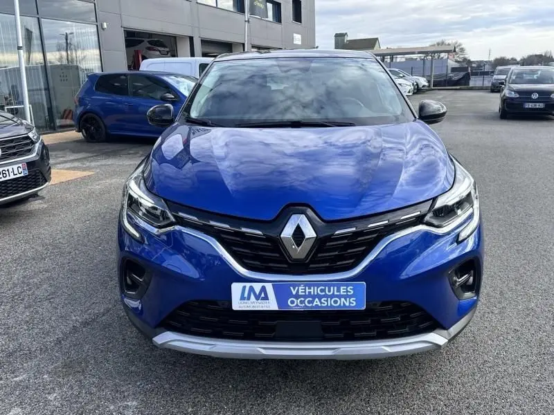 Vue de face d'un Renault Captur bleu métal 2022 avec calandre noire et logo Renault proéminent, sur parking extérieur.