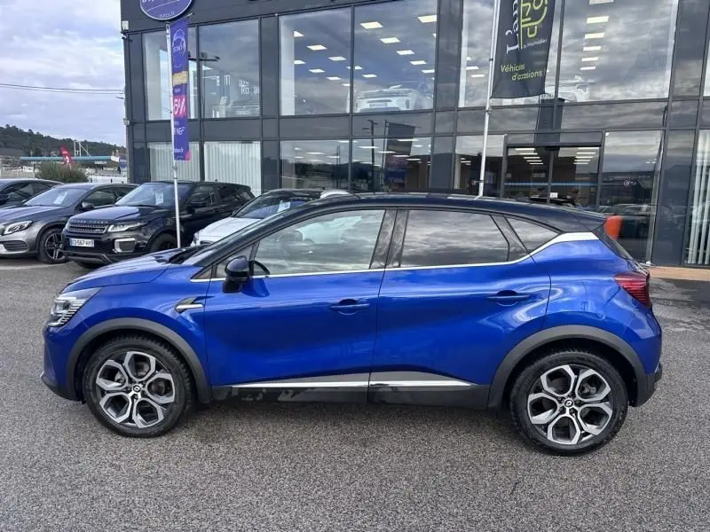 Profil côté gauche du Renault Captur 1.6 E-Tech Hybride 145 Intense bleu métal de 2022 avec toit noir et jantes distinctives.