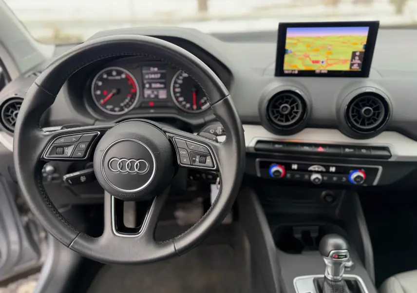 Vue intérieure centrée sur le volant noir d’un Audi Q2 2017 avec tableau de bord et écran GPS en arrière-plan.