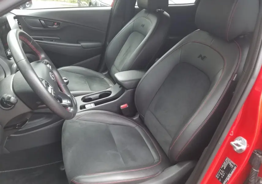 Vue intérieure côté conducteur du Hyundai Kona rouge 2023 avec sièges N Line en Alcantara et cuir noir à surpiqûres rouges.