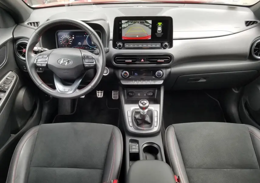 Vue intérieure avant du Hyundai Kona rouge 2023, tableau de bord moderne avec écran central et boîte manuelle.