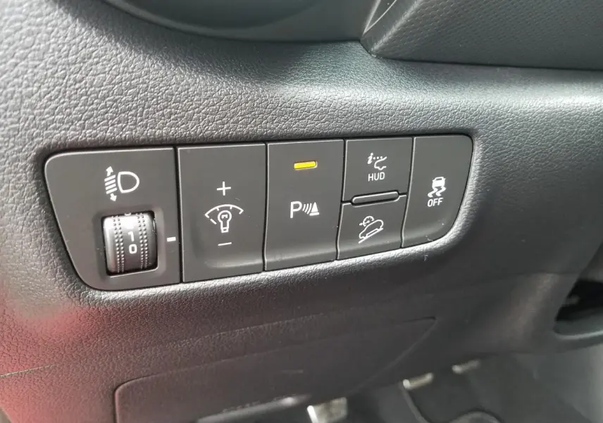 Gros plan sur les commandes intérieures noires du tableau de bord du Hyundai Kona rouge, avec bouton d'aide au stationnement activé.