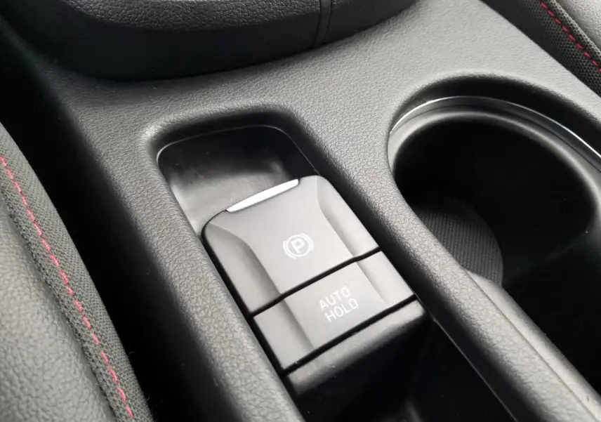 Gros plan sur la commande de frein de parking électrique et auto hold dans l’habitacle noir du Hyundai Kona rouge.