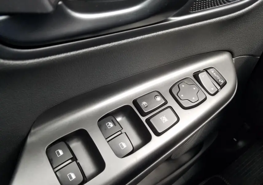 Gros plan sur les commandes de lève-vitres et rétroviseurs côté gauche intérieur du Hyundai Kona rouge 2023.
