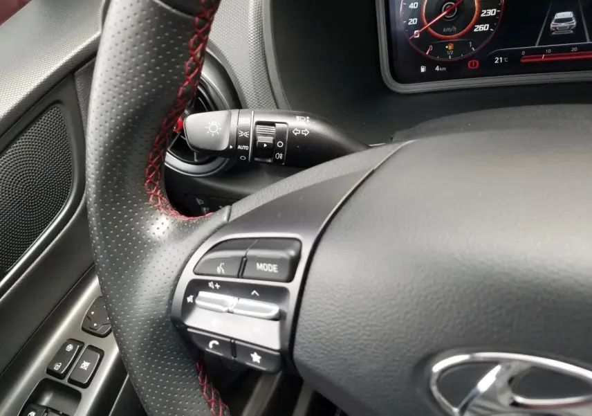 Gros plan sur le volant perforé avec surpiqûres rouges et commandes multifonctions du Hyundai Kona hybride 2023.