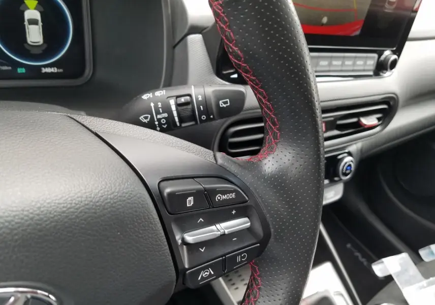 Gros plan sur le volant perforé avec surpiqûres rouges du Hyundai Kona hybride, tableau de bord et écran tactile en arrière-plan.
