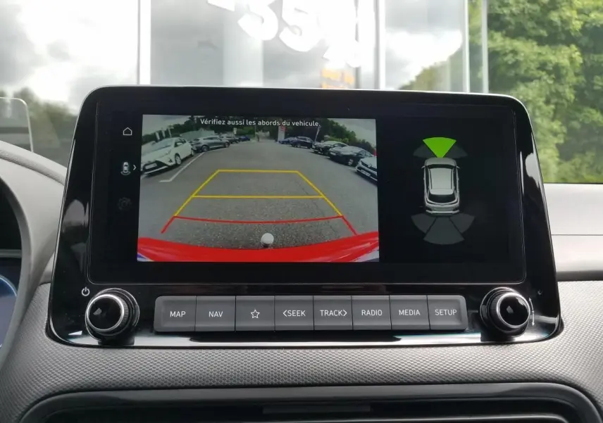 Écran central affichant la caméra de recul du Hyundai Kona rouge, avec guidage de stationnement et capteurs d'obstacles.