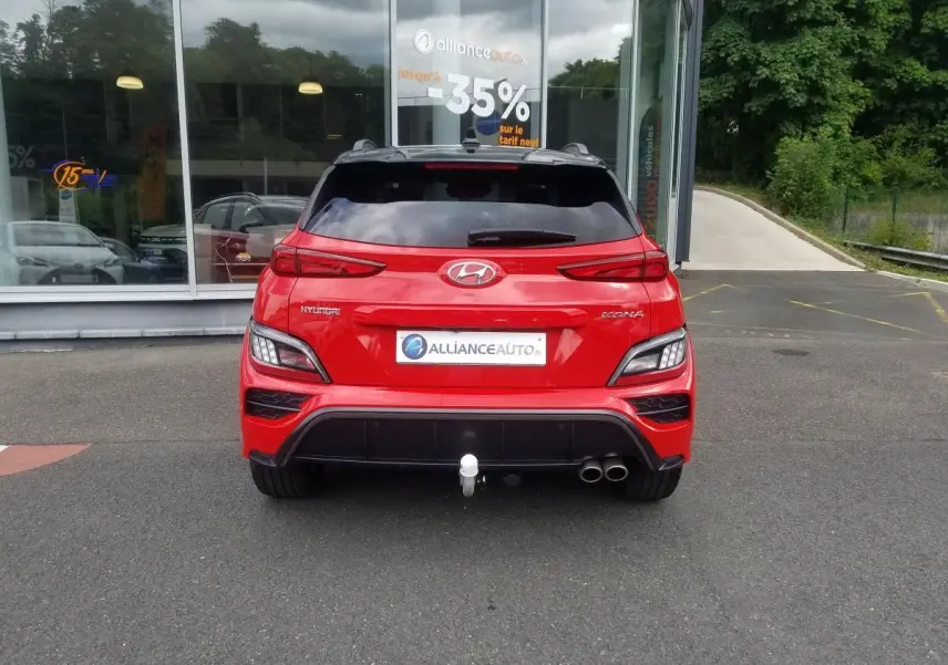 Vue arrière d'un Hyundai Kona rouge 2023 avec toit noir, double sortie d'échappement et attelage visible.