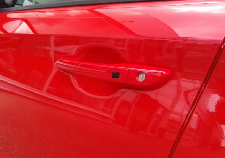 Poignée de porte côté gauche rouge vif d'une Hyundai Kona 2023, finition N Line avec serrure et bouton noir intégré.