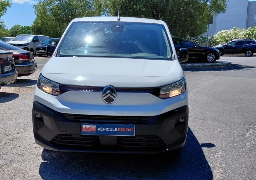 Vue frontale d'un Citroën Berlingo blanc 2025 avec feux allumés et pare-chocs noir sur parking extérieur.