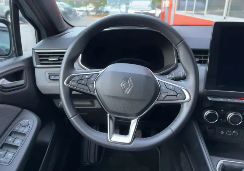 Vue intérieure centrée sur le volant cuir multifonctions de la Renault Clio 2025, avec tableau de bord et commandes visibles.