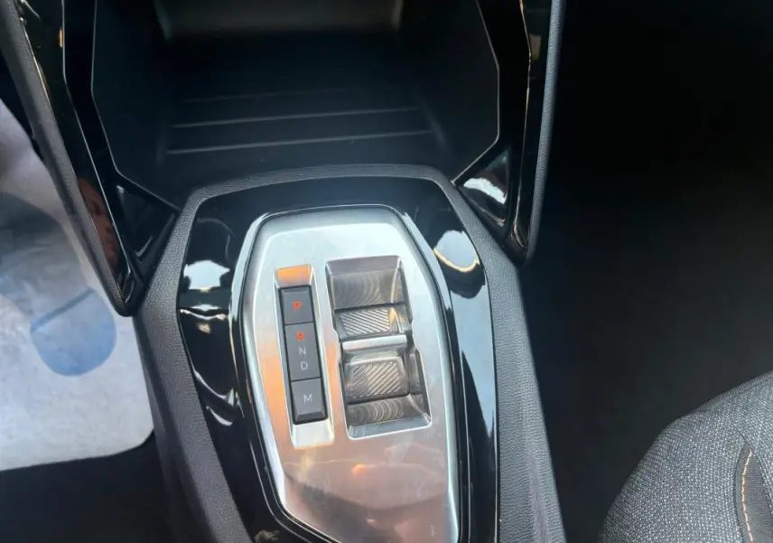Gros plan sur la console centrale du Peugeot 2008 Hybrid 145 gris, montrant la commande de boîte automatique et les commandes de réglage.