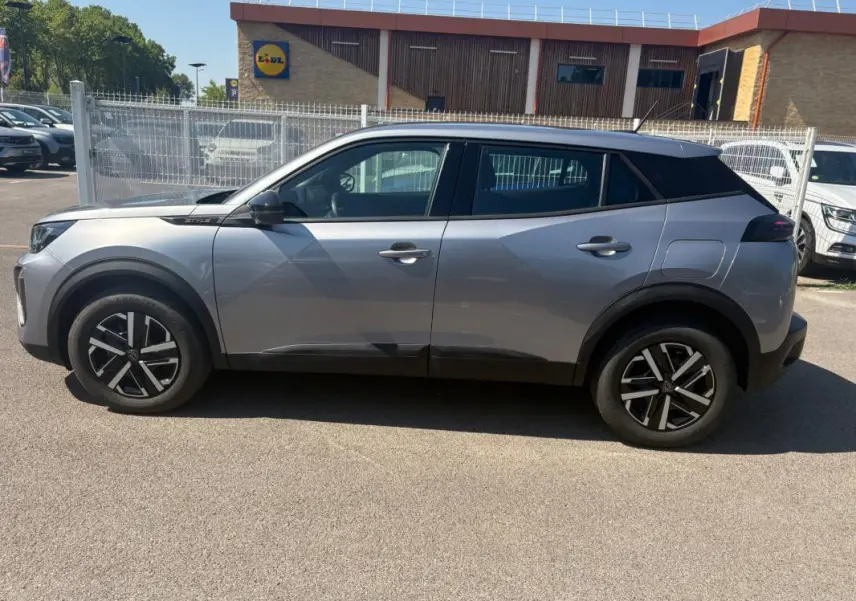 Profil droit d’un Peugeot 2008 Hybrid 145 gris 2025 avec jantes 16 pouces et toit noir contrasté.