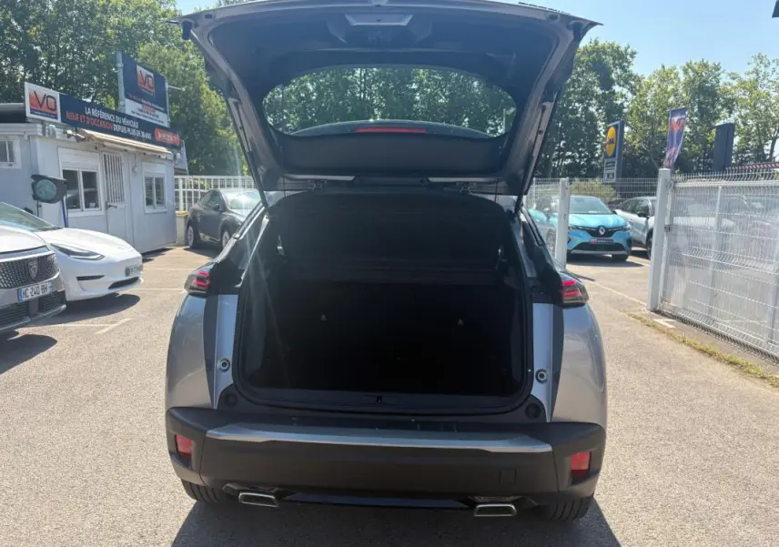 Vue arrière d'un Peugeot 2008 Hybrid 145 gris 2025 avec coffre ouvert et feux arrière allumés en plein jour.