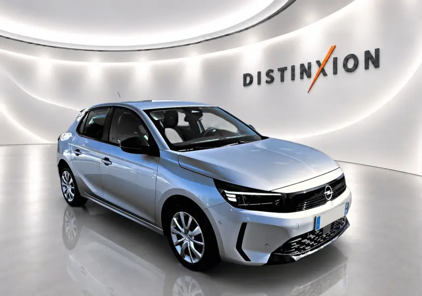 Opel Corsa gris alu vue 3/4 avant droit dans un showroom lumineux avec logo Distinxion en arrière-plan.