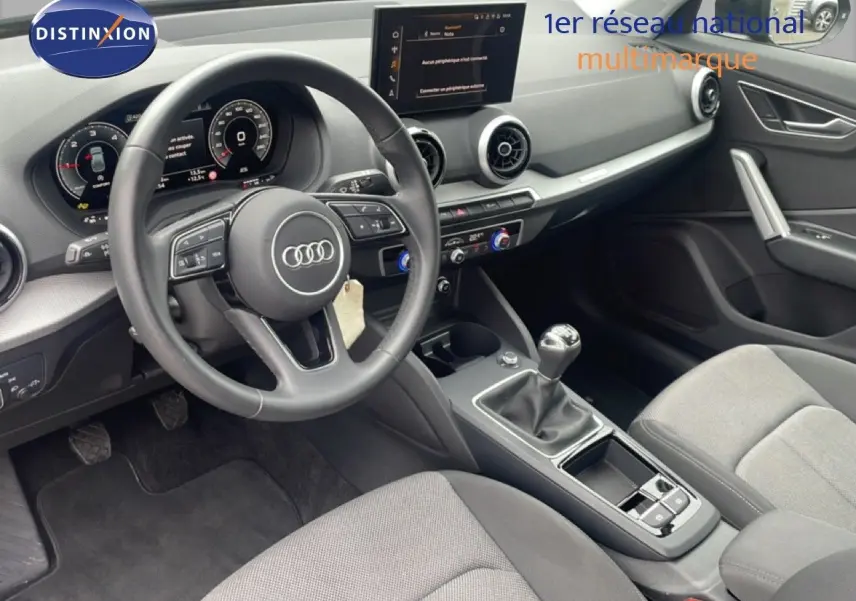 Vue intérieure côté conducteur de l'Audi Q2 30 TDI S-Line 2025, volant cuir, boîte manuelle et tableau de bord digital.