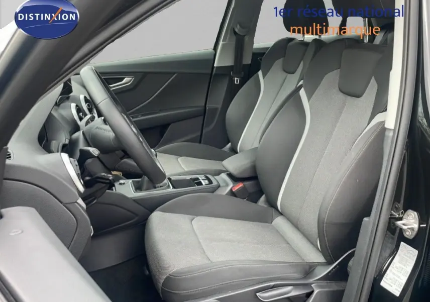 Vue intérieure côté conducteur de l'Audi Q2 30 TDI S-Line 2025, sièges tissu gris et noir, volant cuir multifonction.