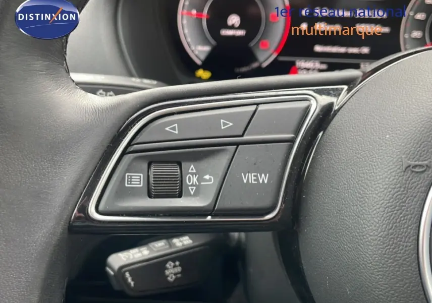 Gros plan sur les commandes au volant côté gauche d’un Audi Q2 noir mito metal, avec tableau de bord numérique en arrière-plan flou.