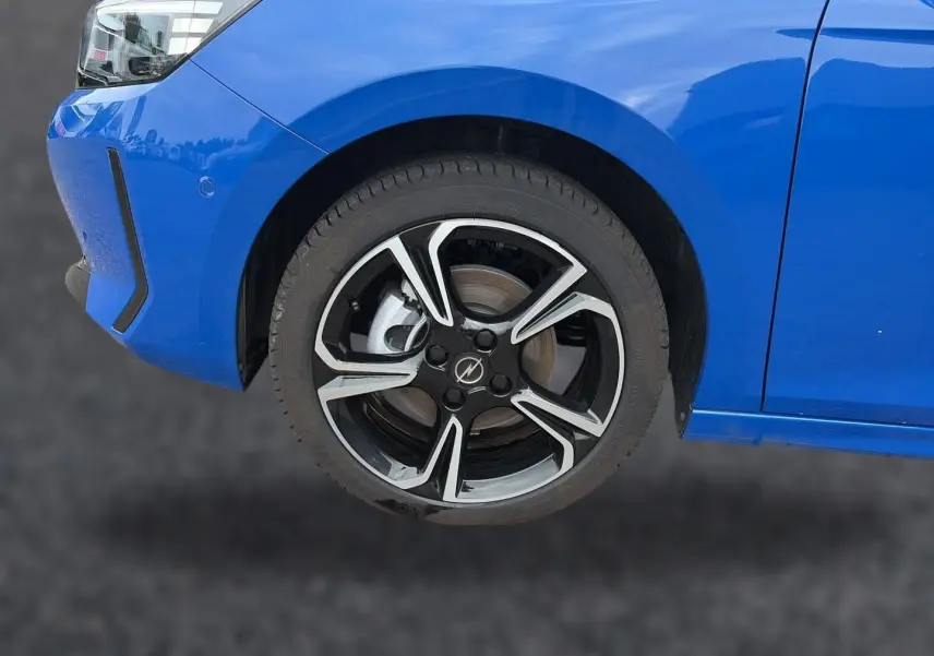 Gros plan sur la roue avant gauche et partie du pare-chocs bleu d'une Opel Corsa 1.2 turbo 100 gs avec jante alu noire et argent.