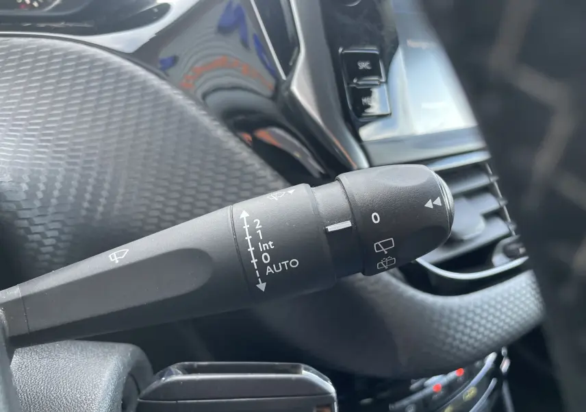 Gros plan sur la commande d'essuie-glace à gauche du volant dans l'habitacle gris-noir du Peugeot 2008 2019.