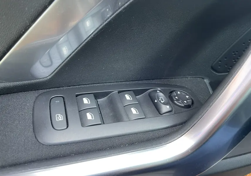 Gros plan sur les commandes de lève-vitres et réglage des rétroviseurs côté conducteur d'un Peugeot 2008 gris 2019.