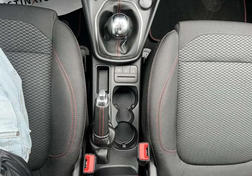 Vue plongeante sur la console centrale du Ford Puma gris Solar, montrant levier de vitesses manuel et sièges noirs à surpiqûres rouges.
