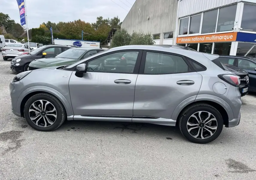 Profil côté gauche du Ford Puma 1.0 EcoBoost mHEV 155 ST Line gris Solar garé en extérieur sur parking.