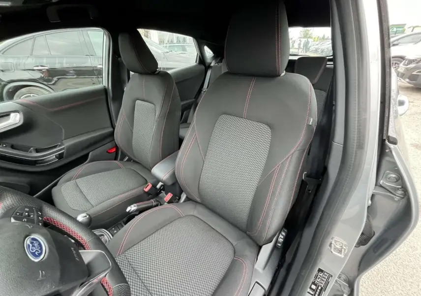 Intérieur avant droit du Ford Puma gris Solar 2023, sièges tissu avec surpiqûres rouges et volant partiellement visible.