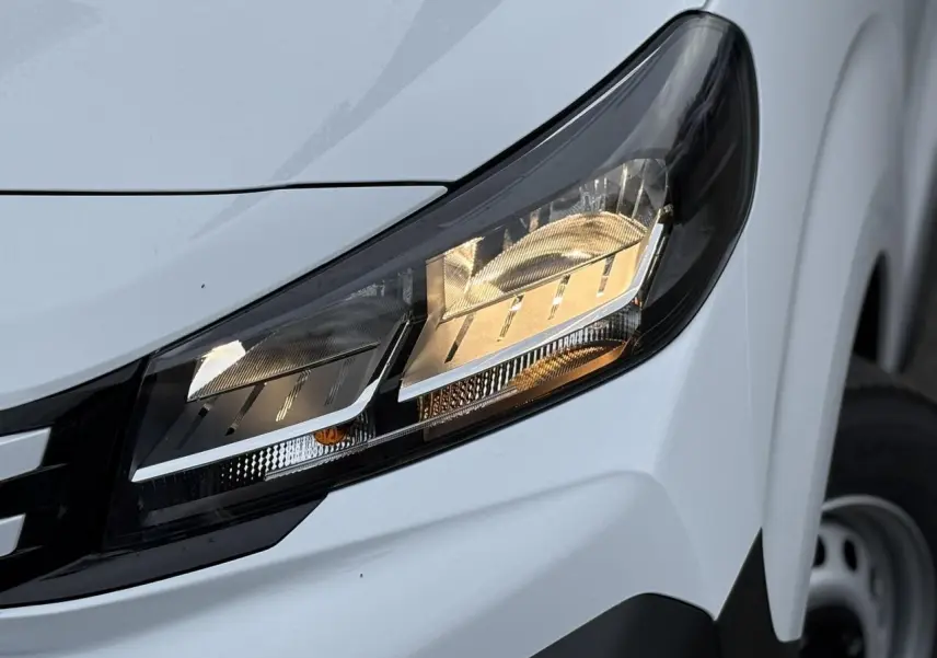 Gros plan sur le phare avant droit du Peugeot Expert Fourgon blanc Icy avec partie de la roue en arrière-plan.