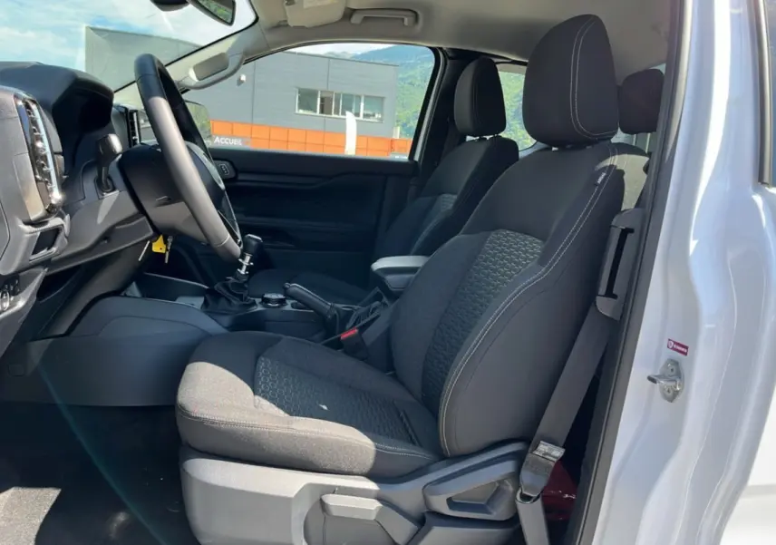 Vue intérieure côté conducteur du Ford Ranger blanc glacier 2025, sièges noirs et volant multifonctions cuir visible.