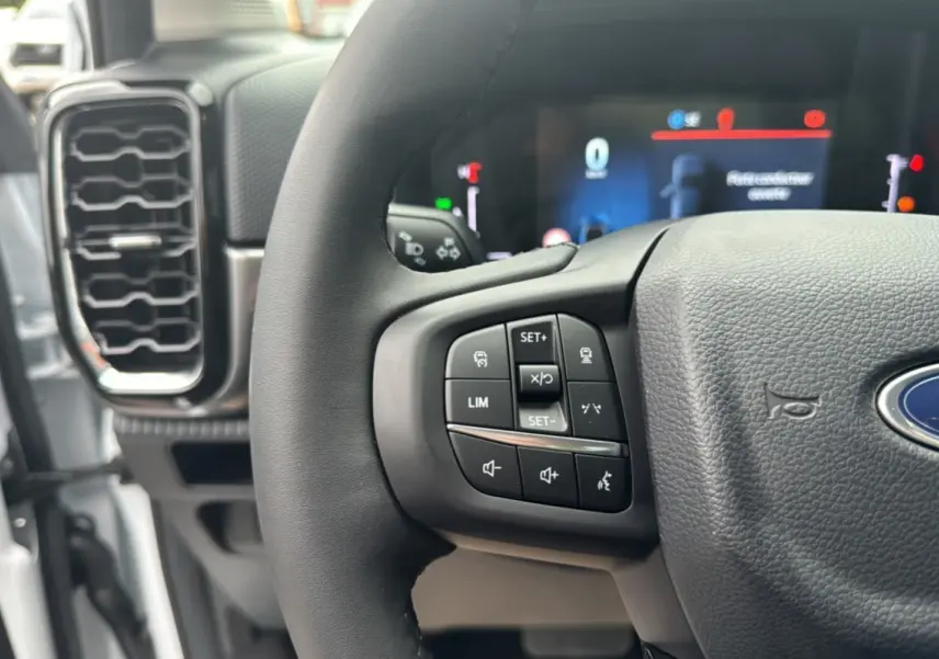 Gros plan sur le volant multifonctions noir du Ford Ranger 2025 avec commandes au volant et tableau de bord numérique flou.