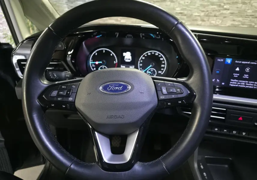 Vue rapprochée du volant noir en cuir du Ford Transit Connect 2023 avec tableau de bord et écran tactile visibles.