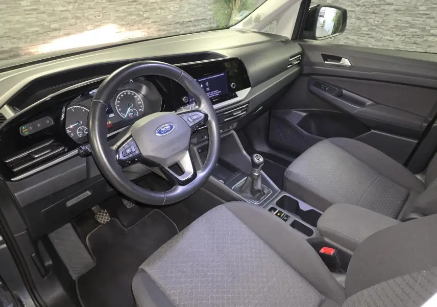 Vue intérieure côté conducteur du Ford Transit Connect gris 2023, volant cuir, boîte manuelle et console centrale moderne.