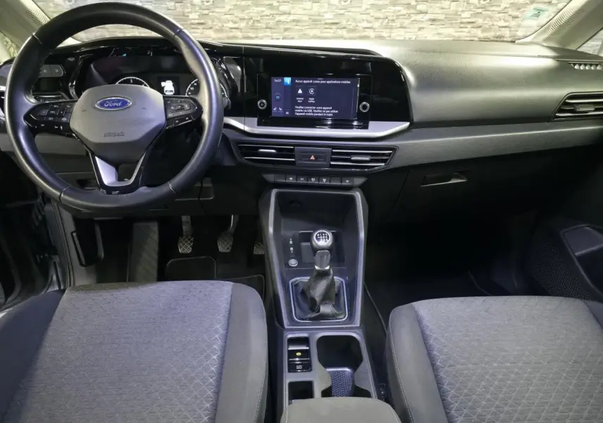 Vue intérieure avant du Ford Transit Connect gris 2023, volant cuir, tableau de bord noir avec écran tactile central.