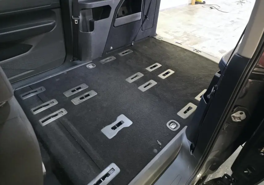 Vue intérieure arrière côté droit du Ford Transit Connect gris, montrant le plancher avec fixations de sièges et porte coulissante ouverte.