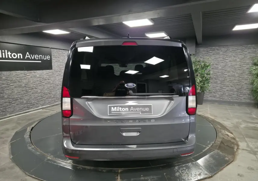 Vue arrière d'un Ford Tourneo Connect gris métallisé dans un showroom avec hayon vitré et feux rouges verticaux.