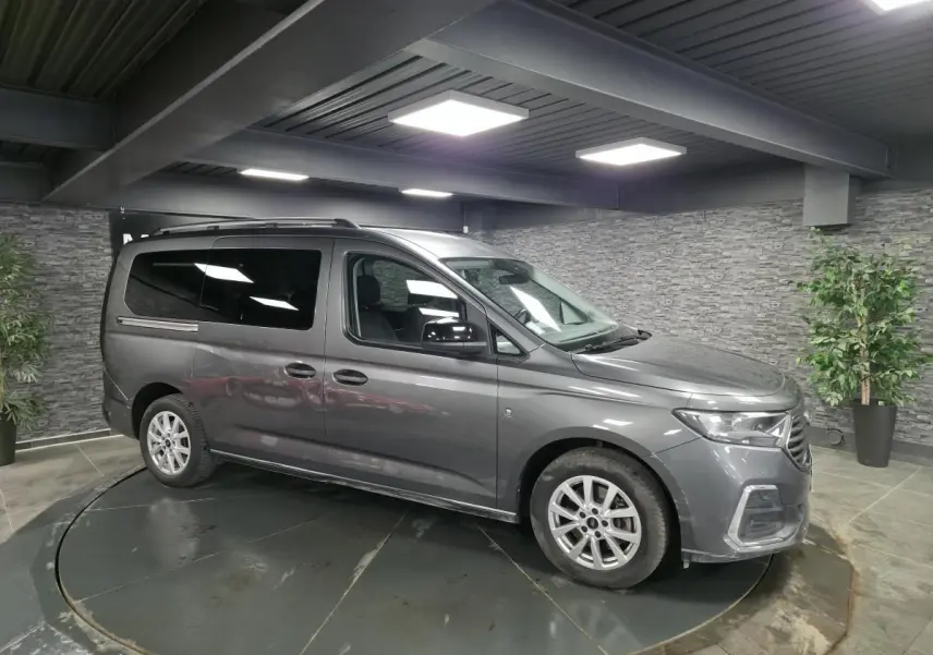 Vue 3/4 avant droit du Ford Transit Connect Tourneo gris métallisé, avec barres de toit argentées et vitres arrière surteintées.