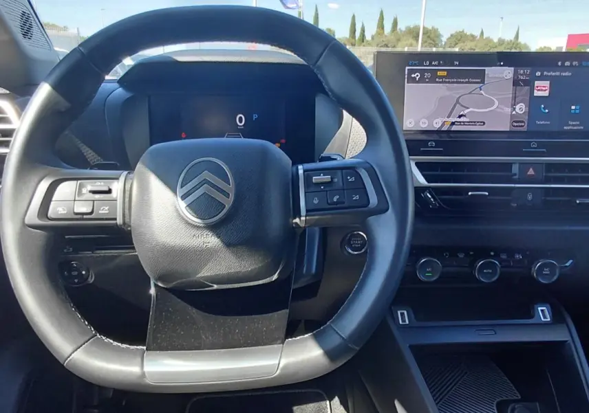 Vue intérieure centrée sur le volant cuir et le tableau de bord numérique du Citroën C4 X noir 2025 hybride.