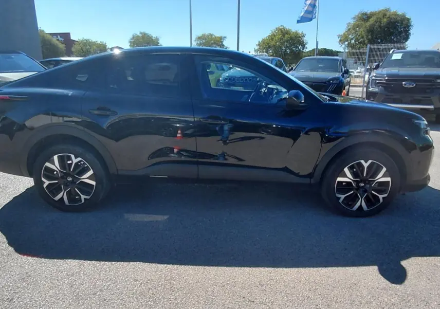 Vue de profil côté gauche d'une Citroën C4 X noire 2025 avec jantes alliage 17 pouces sur parking extérieur.