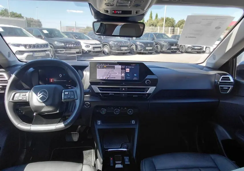 Vue intérieure avant du Citroën C4 X noir 2025, montrant le tableau de bord moderne et le volant cuir avec commandes intégrées.