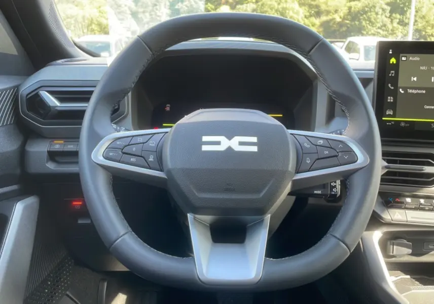 Vue rapprochée du volant cuir noir et du tableau de bord digital du Dacia Bigster Hybrid 150 4x4 gris schiste.