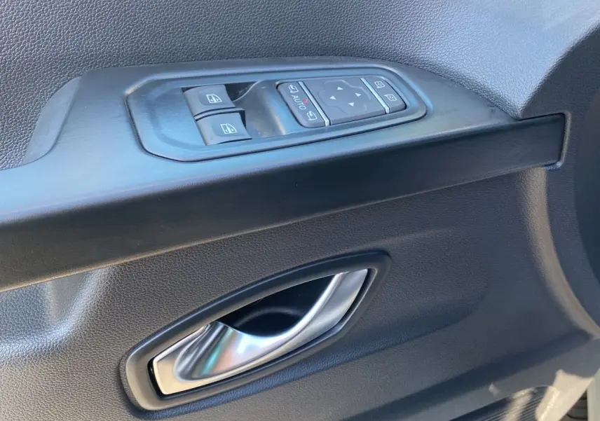 Poignée intérieure et commandes électriques de la porte avant gauche du Renault Trafic Combi gris Highland 2025.